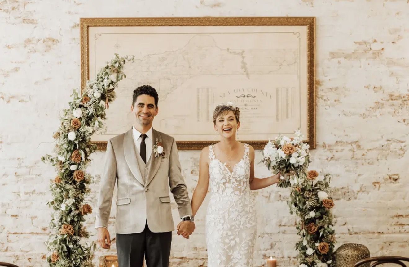 A couple in front of a floral arch and a large gilt frame